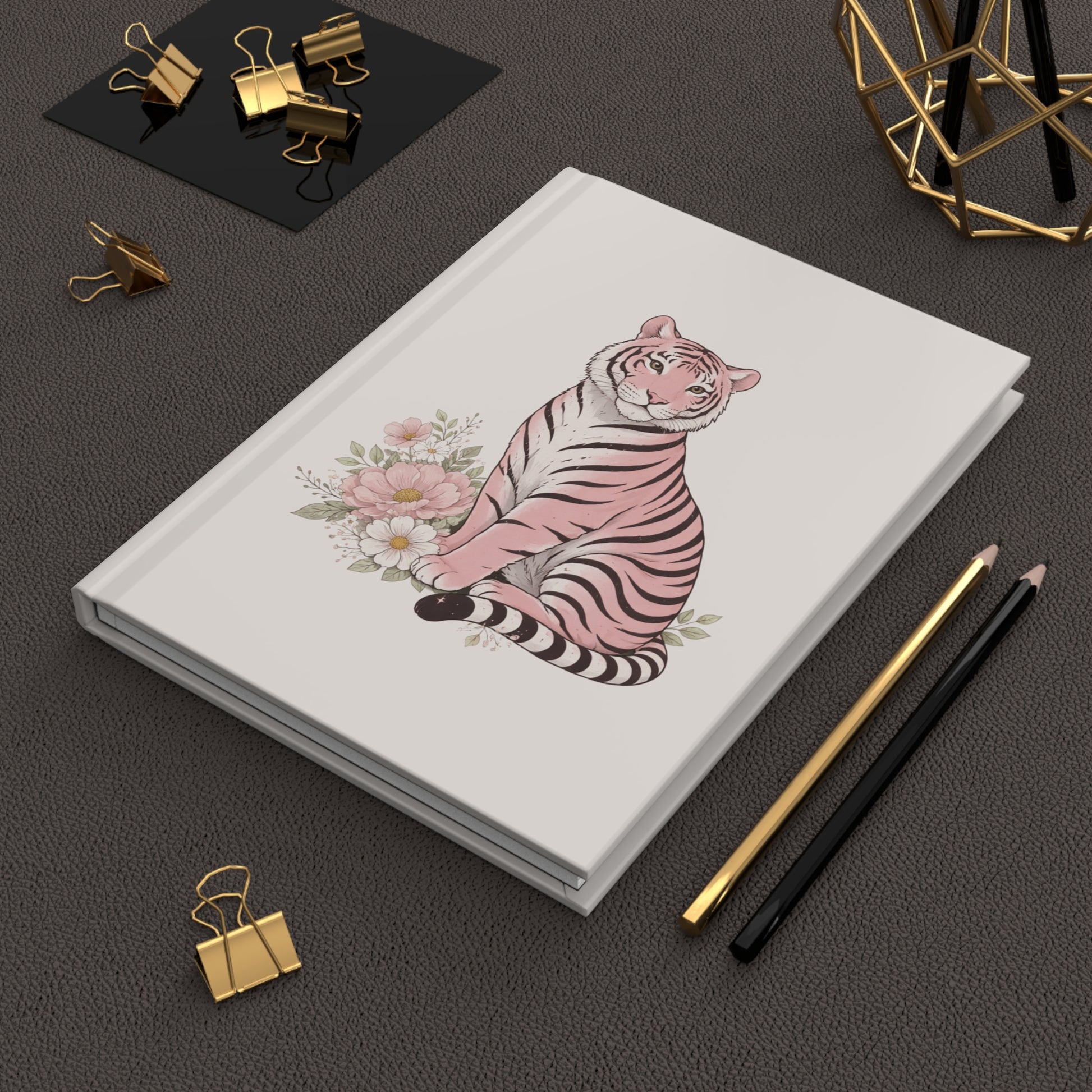 A soft, feminine hardcover journal featuring a pink tiger sitting among pastel flowers on a clean cream background sitting on a desk.