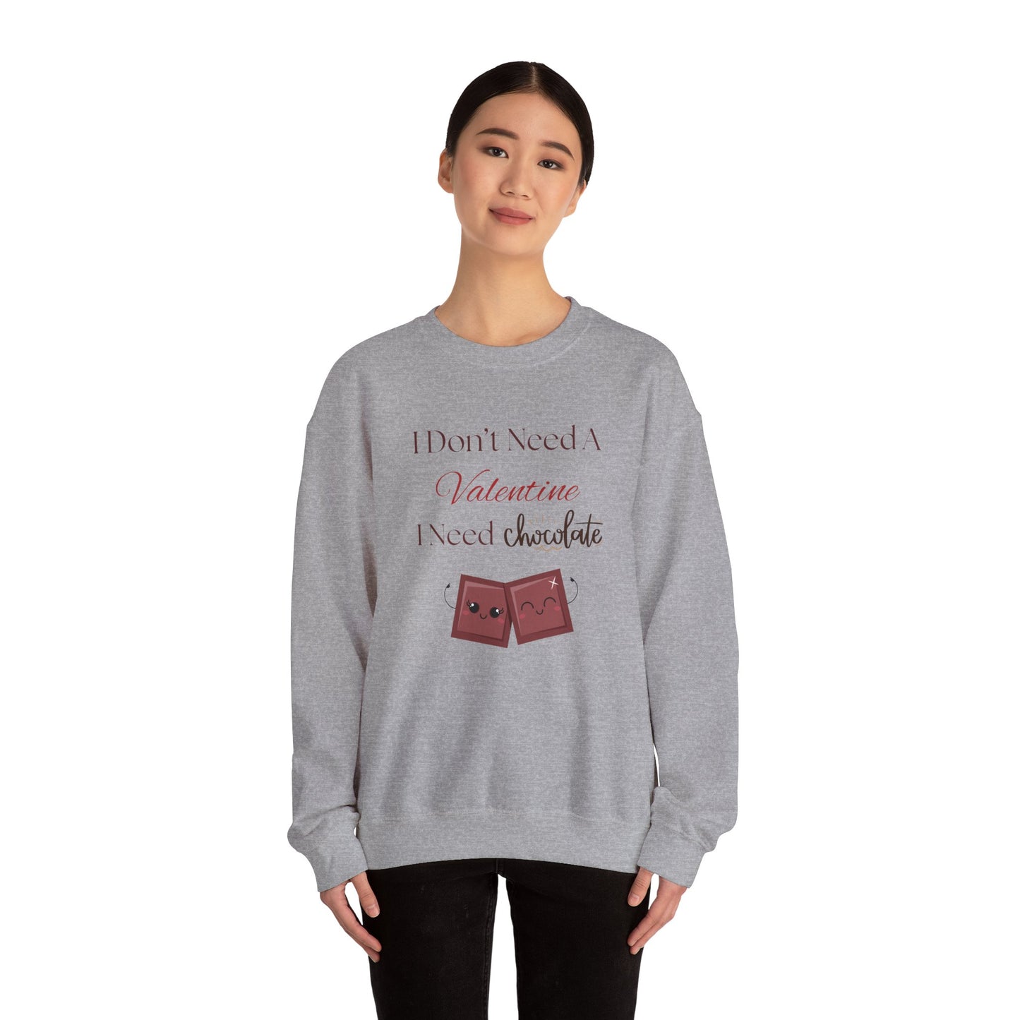 A woman wearing a gray Valentine’s sweatshirt that says “I Don’t Need a Valentine, I Need Chocolate,” featuring two cute smiling chocolate characters at the bottom.