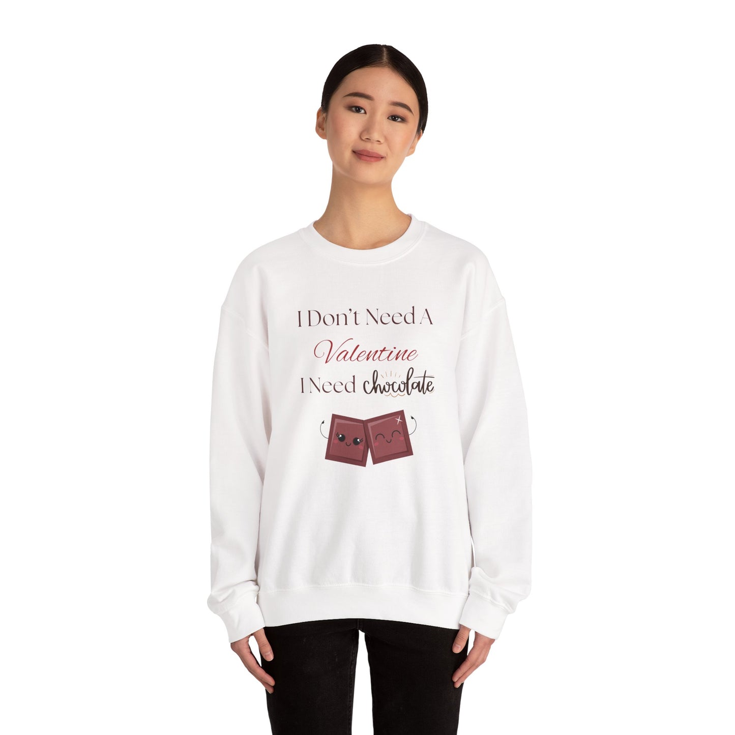 A woman wearing a white Valentine’s sweatshirt that says “I Don’t Need a Valentine, I Need Chocolate,” featuring two cute smiling chocolate characters at the bottom.