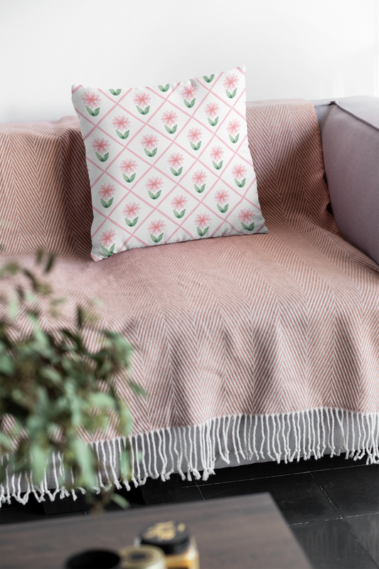 A soft pink daisy-patterned throw pillow with insert resting on a blush herringbone blanket on a cozy sofa.