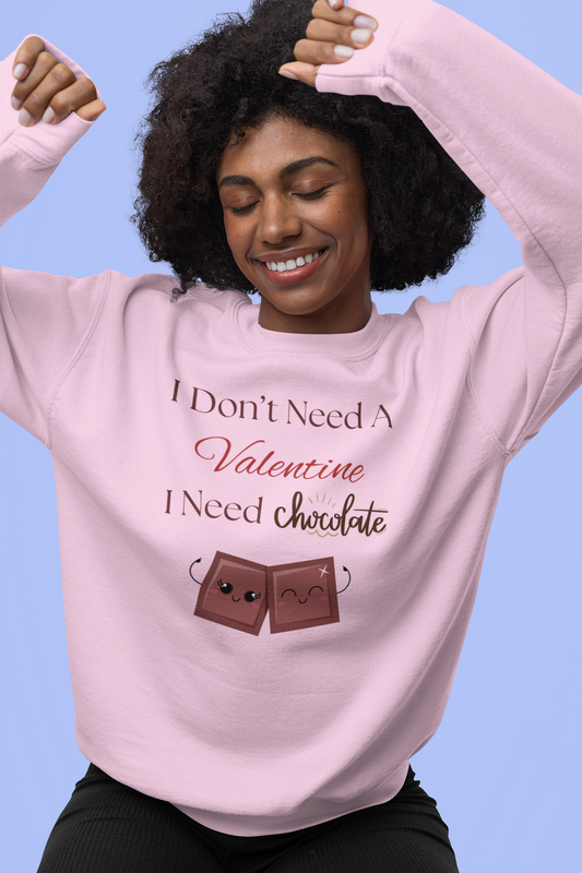 A woman wearing a light pink Valentine’s sweatshirt that says “I Don’t Need a Valentine, I Need Chocolate,” decorated with two cute smiling chocolate characters.