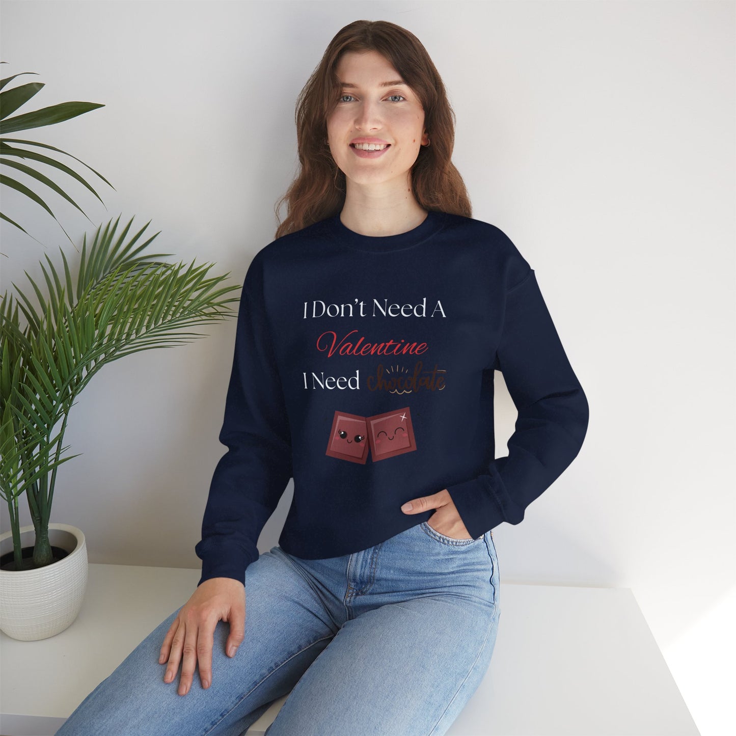 A woman wearing a navy blue Valentine’s sweatshirt that says “I Don’t Need a Valentine, I Need Chocolate,” featuring two cute smiling chocolate characters at the bottom.